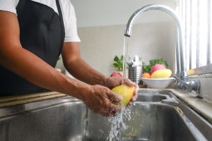 person in apron washing a mango under a sink